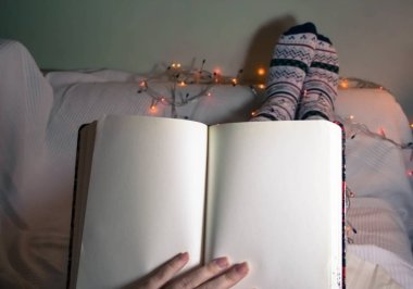 Female makes notes sitting on the sofa, writes in diary in christmas socks with garland