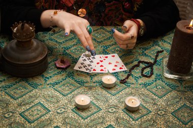 Çingene falcı kız sihirli özelliklerle masanın yanında duruyor: mumlar, kartlar, tütsü vs..