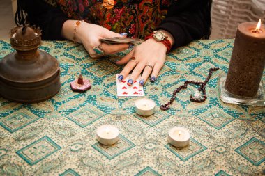 Çingene falcı kız sihirli özelliklerle masanın yanında duruyor: mumlar, kartlar, tütsü vs..