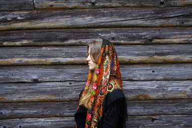 Siyah paltolu güzel bir kız ve köydeki ahşap bir duvarın arkasında geleneksel bir şablon olan Rus halk atkısı. Geleneklerin korunması