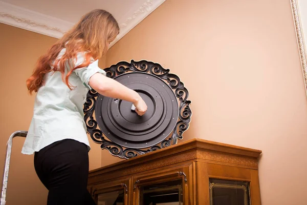 Young woman changing battery in a clock on the wall