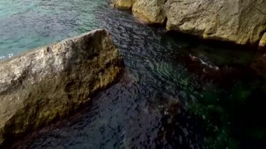 Dalgalar, deniz / okyanus kıyısındaki büyük kayaların üzerinden mavi suyun etrafında akar. Shalyapin mağarasında taş plajı Noviy Svet, Kırım 'daki Golitsyn patikasında.