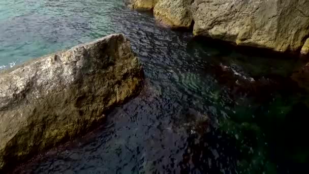 波は海や海岸の大きな岩の上に青い水の周りを流れます シャリアピン グロテトの石のビーチ クリミア スヴェットのゴリツィン トレイル — ストック動画