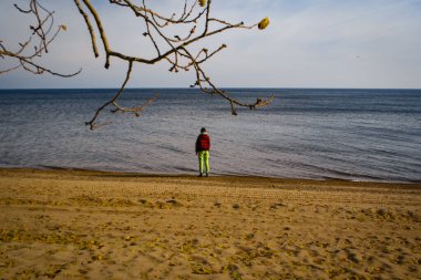 Kız, güneşli bir sonbahar gününde gölün kumlu kıyısında duruyor.