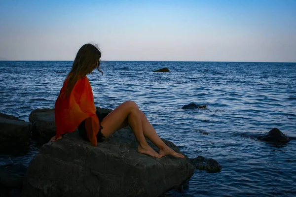 La fille est assise sur un rocher dans la mer et regarde le coucher du soleil — Photo