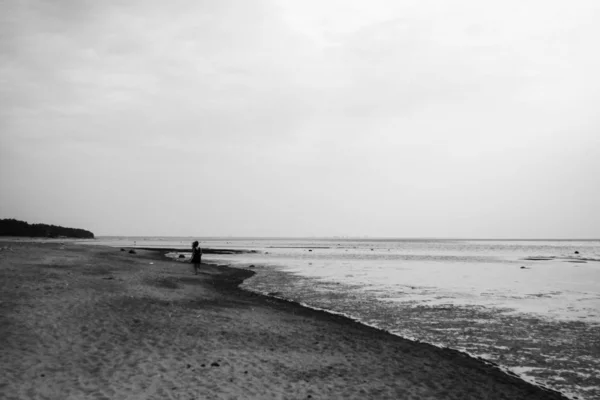 Girl in the distance runs along the seashore on cloudy summer day in black and white