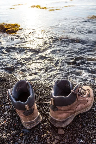 Par de botas turísticas em uma costa do mar — Fotografia de Stock