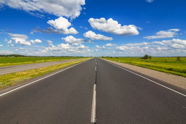 Długo asfaltową drogą przez zielone pola — Zdjęcie stockowe