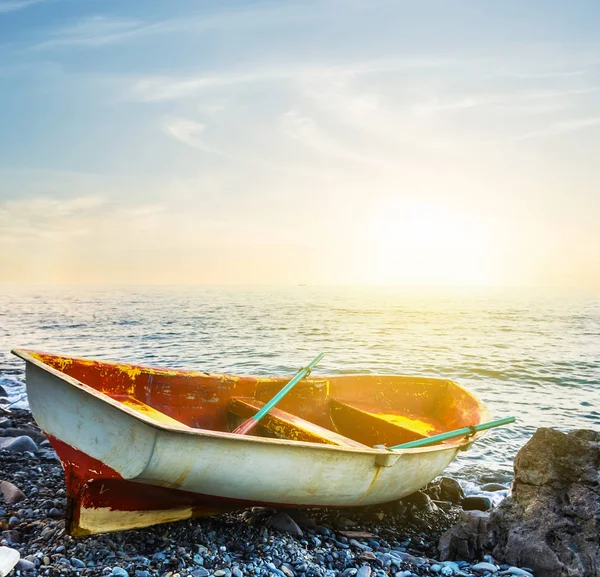 Small boat on a stony sea coast at the sunset — Stock Photo, Image