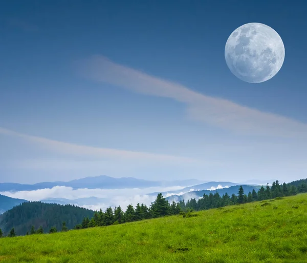 Lua cheia em um céu acima de umas colinas verdes — Fotografia de Stock