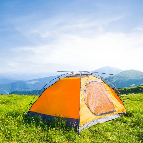 Oranje toeristische tent onder een groene heuvels op de vroege ochtend — Stockfoto