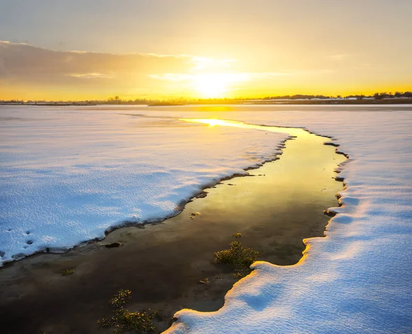 夕日を積雪の海岸の間で小さな溶かし川 — ストック写真