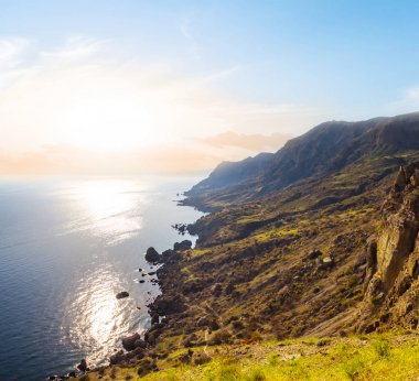 bir gün batımı bir deniz üzerinde bir Dağı yamaç görüntülemek.