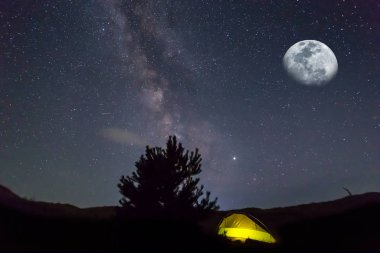 Yıldızlı bir gökyüzünün altında sarı turistik çadır ve yarım ay, dış seyahat arka planı.