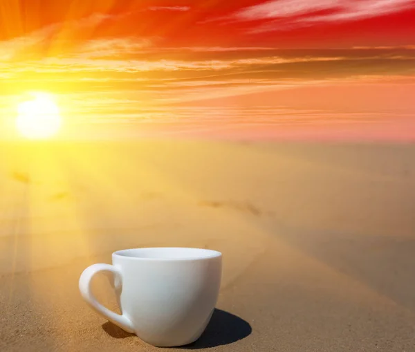 closeup porcelain coffee cup on the sand at the dramatic sunset, stylized coffee background