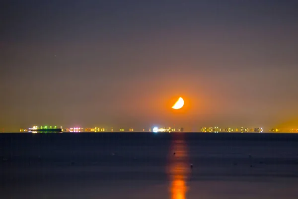 half moon rising above sea port