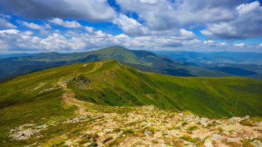 Bulutlu gökyüzünün altındaki yeşil dağ omurgası