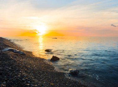 Güneşin doğuşunda deniz taşlı plajı, sabahın erken saatlerinde deniz manzarası.