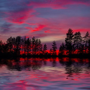 Dramatik alacakaranlık sahnesi, gölde yansıtılan bulutlu bir gökyüzünde orman silueti.
