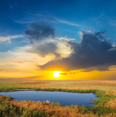 Gün batımında bir çayırın ortasında küçük bir göl