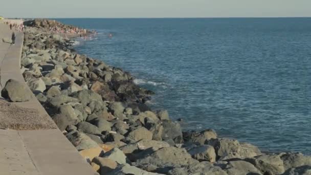 Slow tilt of rocky sea shore with beach and tourists. — Stock Video