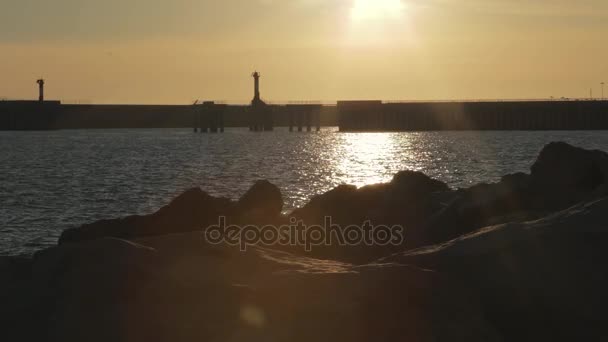 Rotsachtige kust met pier in de achtergrond in zonsondergang verlichting. — Stockvideo