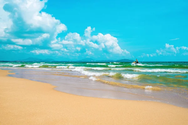 Göz kamaştırıcı sarı kumsal, masmavi deniz ve güzel bulutlu mavi gökyüzü. Uzakta, denizde jet ski süren bir adam. Güney Çin Denizi. Hainan Cennet Adası, Sanya Şehri. Beach Haitang Körfezi.