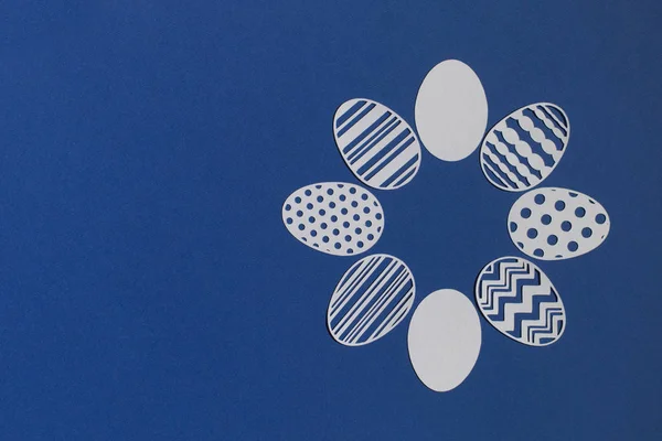 Klasik mavi arka planda kağıttan kesilmiş Paskalya yumurtaları.