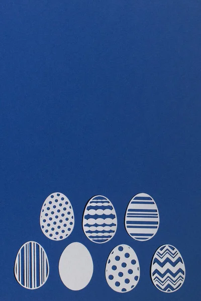 Klasik mavi arka planda kağıttan kesilmiş Paskalya yumurtaları.