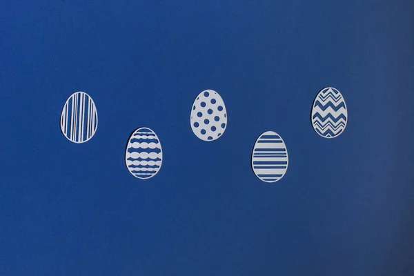 Klasik mavi arka planda kağıttan kesilmiş Paskalya yumurtaları.