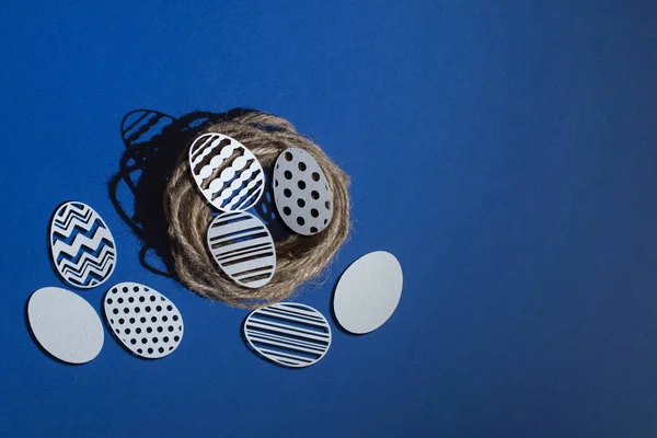 Klasik mavi bir arka planda jute yuvasına oyulmuş Paskalya kağıdı yumurtaları.