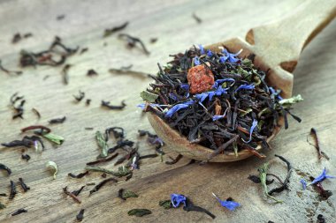 Karışık çay. Kuru çiçek yaprakları ve meyveli siyah çay. Tahta kaşıkta kuru siyah çay yaprakları. Kapat.