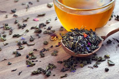 Karışık çay. Kuru çiçek yapraklı yeşil çay. Tahta kaşıkta kuru yeşil çay yaprakları ve bir bardak yeşil çay. Kapat.