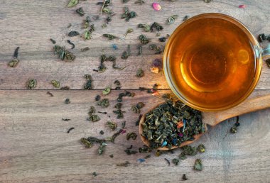 Karışık çay. Kuru çiçek yapraklı yeşil çay. Tahta kaşıkta kuru yeşil çay yaprakları ve bir bardak yeşil çay. Kapat.