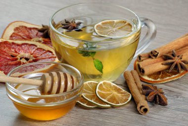 Bal ve çay. Bir bardak limonlu bitki çayı, bal, kurutulmuş narenciye, anason yıldızları ve ahşap bir masada tarçın çubukları. Soğuk algınlığı ve grip için sıcak çay. 