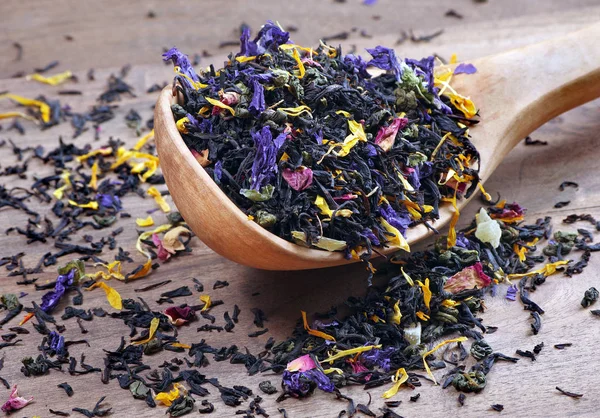 blended tea. black tea with dry flower petals and fruits. dry black tea leaves in a wooden spoon. close up