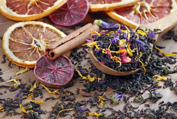 blended tea. black tea with dry flower petals and citrus fruits. dry black tea leaves in a wooden spoon. close up