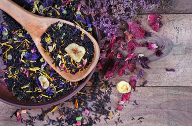 Çiçek yapraklarıyla karıştırılmış çay ve tahta kaşıkta kurutulmuş meyve. Kapat.