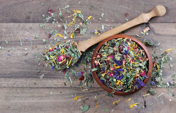 medicinal herbs in a wooden bowl. dry mint, hibiscus flowers, calendula petals, forest mallow flowers and fruit slices in a bowl on a wooden table. herbal vitamin tea. blended herbal tea.