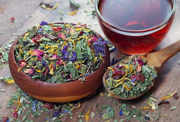 herbal tea in a wooden bowl and a cup of fresh herbal tea. dry mint, hibiscus flowers, calendula petals, forest mallow flowers and fruit slices on a wooden table. herbal vitamin tea