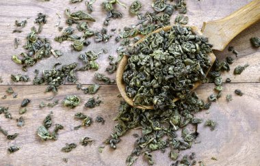 Tahta bir masada, tahta bir kaşıkta yeşil çay yaprakları..