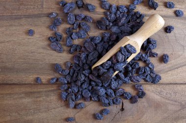 Tahta bir masada kepçedeki siyah kuru üzümler. Bir yığın siyah kuru üzüm. en üstteki görünüm