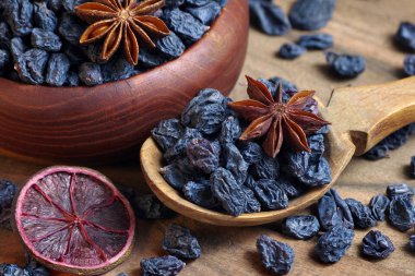 Tahta bir masanın üzerindeki kasede siyah kuru üzümler. Siyah kuru üzüm, tarçın ve anason yıldızları yaklaşın.