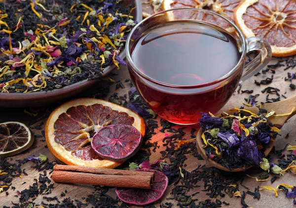 cup of fresh tea and different varieties of tea leaves on a wooden table. blended tea with flower petals, and dried citruses.