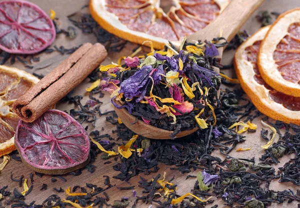 blended tea. black tea with dry flower petals and citrus fruits. dry black tea leaves in a wooden spoon. close up