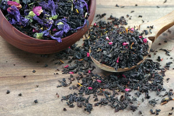 blended tea. black tea with dry flower petals. dry black tea leaves in a wooden spoon. close up