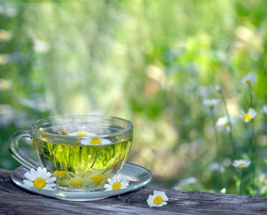 Çiçek açan bir tarlanın arka planında, ahşap bir masada bir fincan papatya çayı. Bitki çayı. Boşluğu kopyala