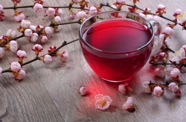 Tahta bir masanın üzerinde bir fincan amber çayı ve sakura çiçeği.