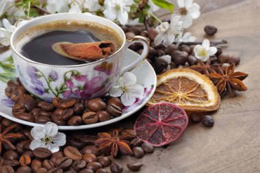 Bir fincan kahve, kavrulmuş kahve çekirdekleri, baharatlar ve sakura çiçekleri ahşap bir masada. Boşluğu kopyala