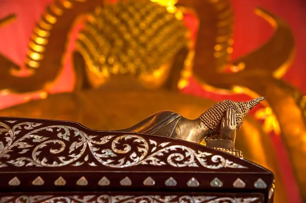 STILL LIFE OF RECLINING BUDDHA STATUES. Bronze Buddha statue in reclining posture with right hand supporting the head, lying on a rosewood bed with pearl inlay. In front, there is another Buddha statue out of focus.